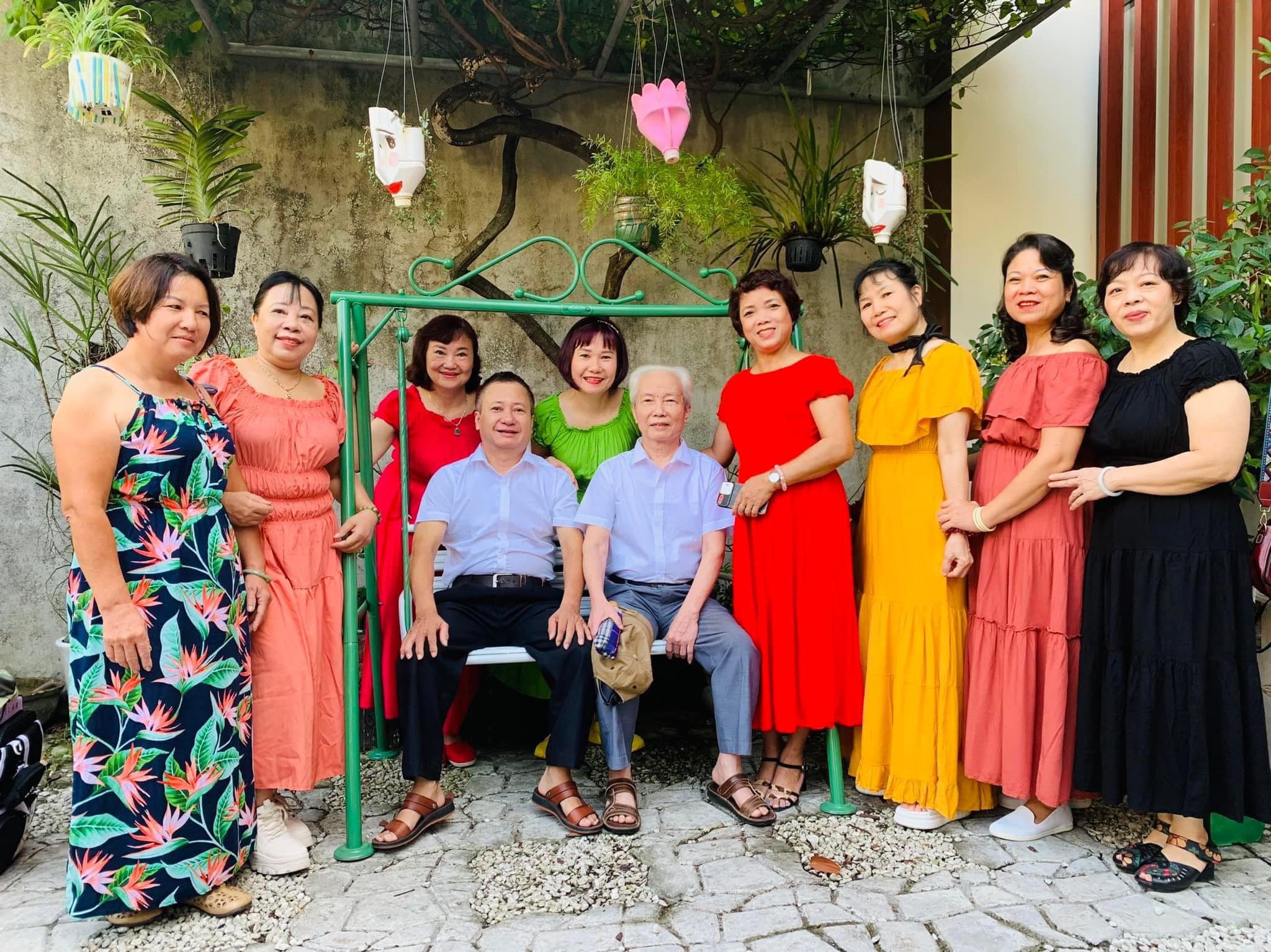 Gia đình chụp ảnh kỷ niệm trong khu vườn homestay tại Huế với nhiều cây xanh và xích đu, mọi người mặc trang phục nhiều màu sắc.