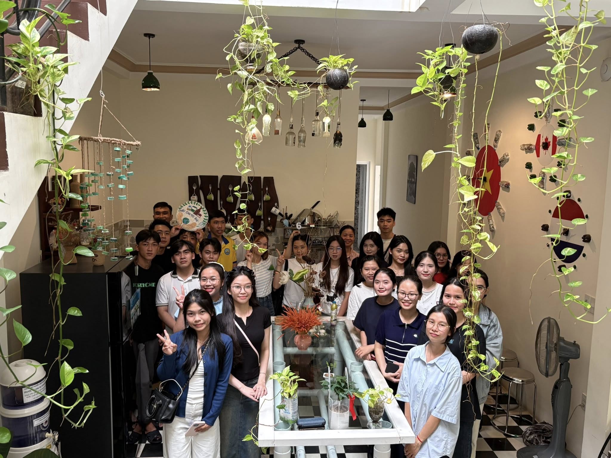 Nhóm bạn trẻ chụp ảnh trong không gian sinh hoạt chung của homestay tại Huế với nhiều cây xanh treo và bàn sinh hoạt lớn.